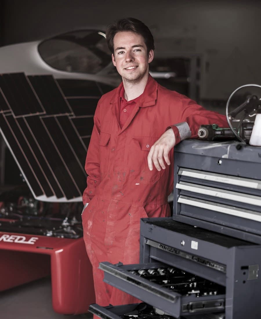Technicien Mécanov en combinaison rouge, adossé à sa servante d’outillage dans l’atelier